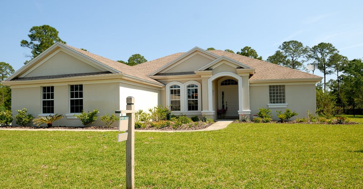 Beautiful suburban house with lush lawn, showcasing a for sale sign under a clear blue sky.
